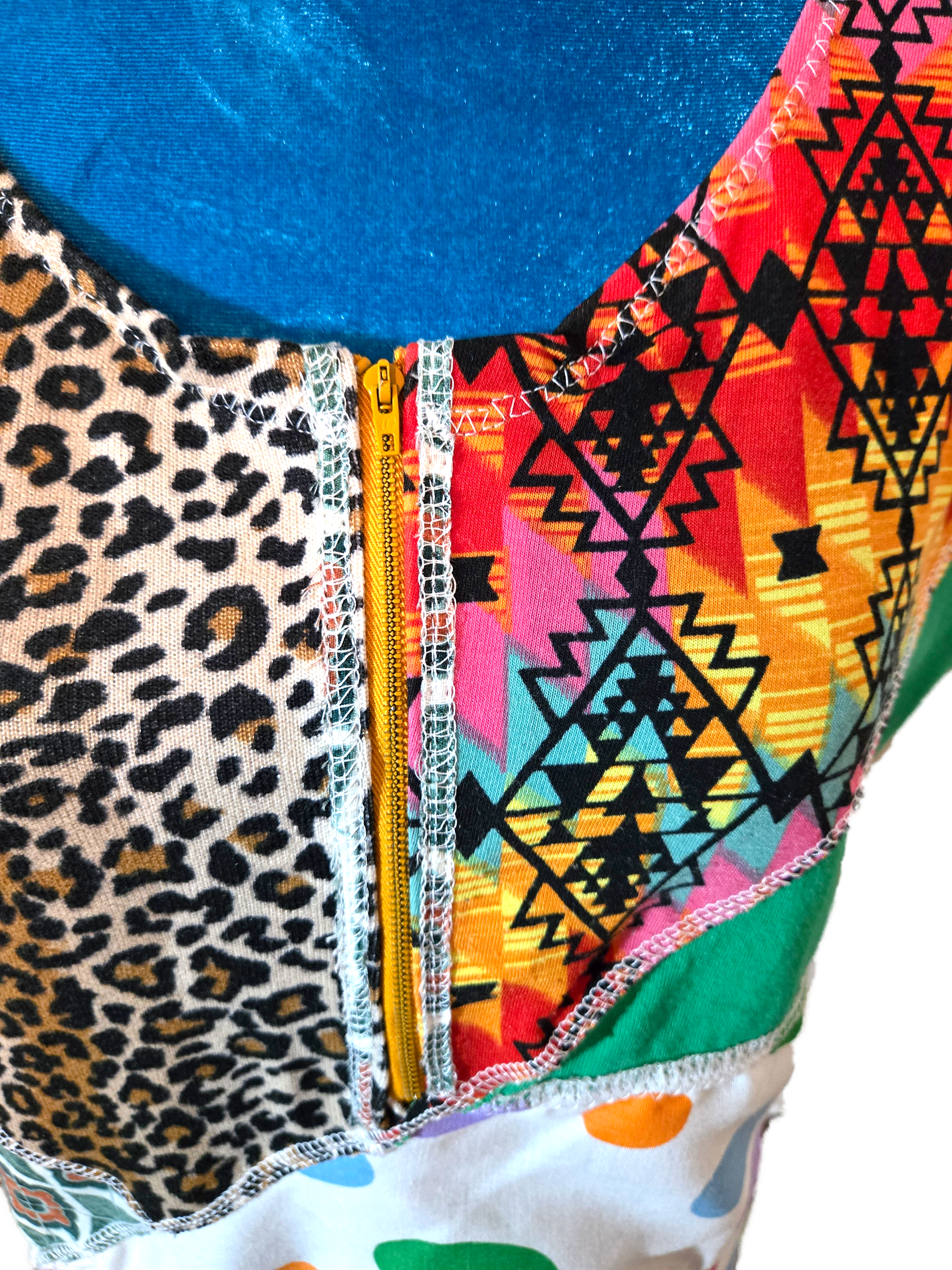 Close-up of a colorful fabric with leopard print, geometric patterns on a blue manniquin with a white background.