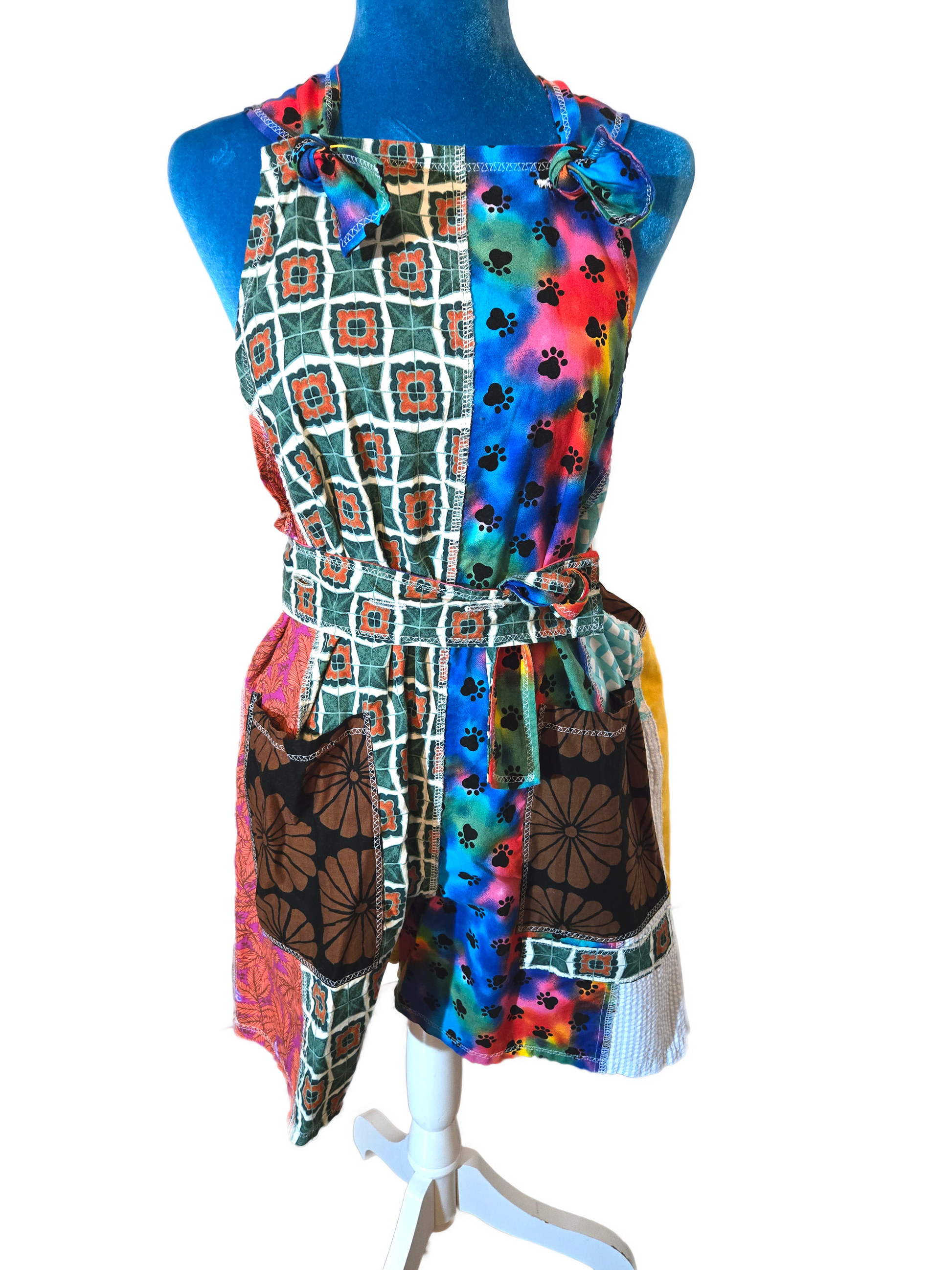 Colorful patchwork romper front view. Features a belt and multi-color tie dye and green prints. Print on the right includes tie dye and paw prints. Center pant portion has large contrasting pockets