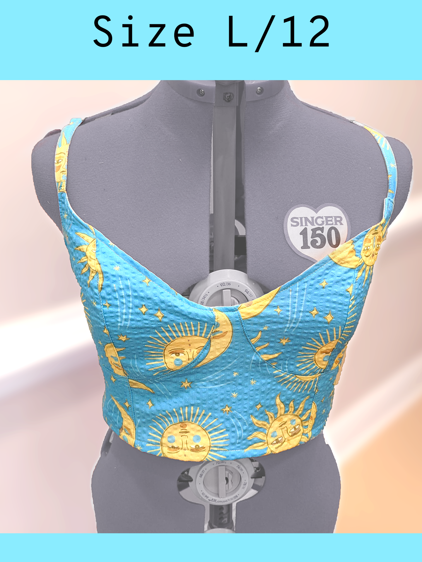 A light blue cropped tank top with a yellow sun and moon print and gold topstitching, displayed on a mannequin. With a text overlay that reads, "Size L/12".