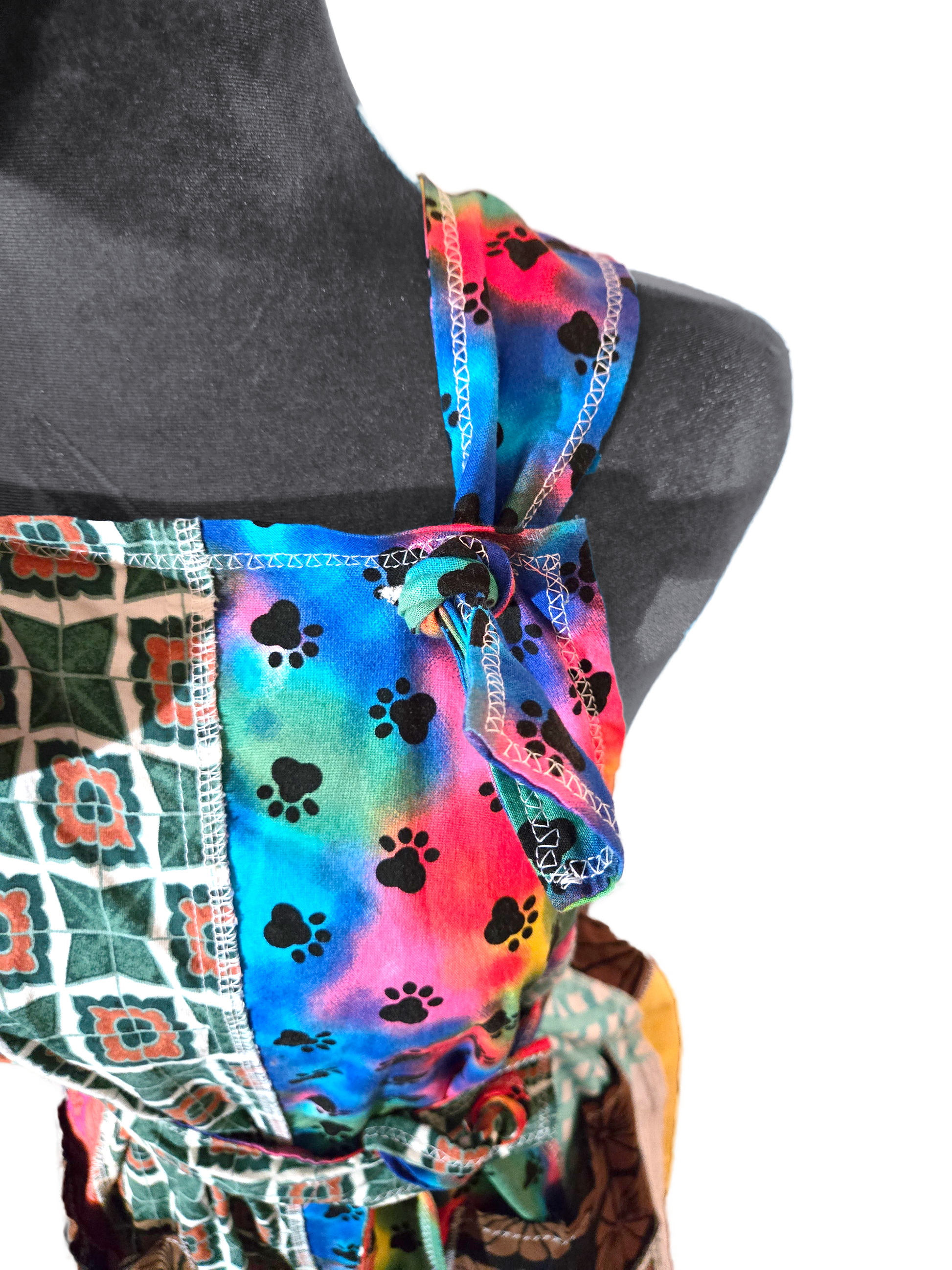 Colorful romper top on a manniquin. Zoomed into straps which thread through a buttonhole and are knotted to keep secure.