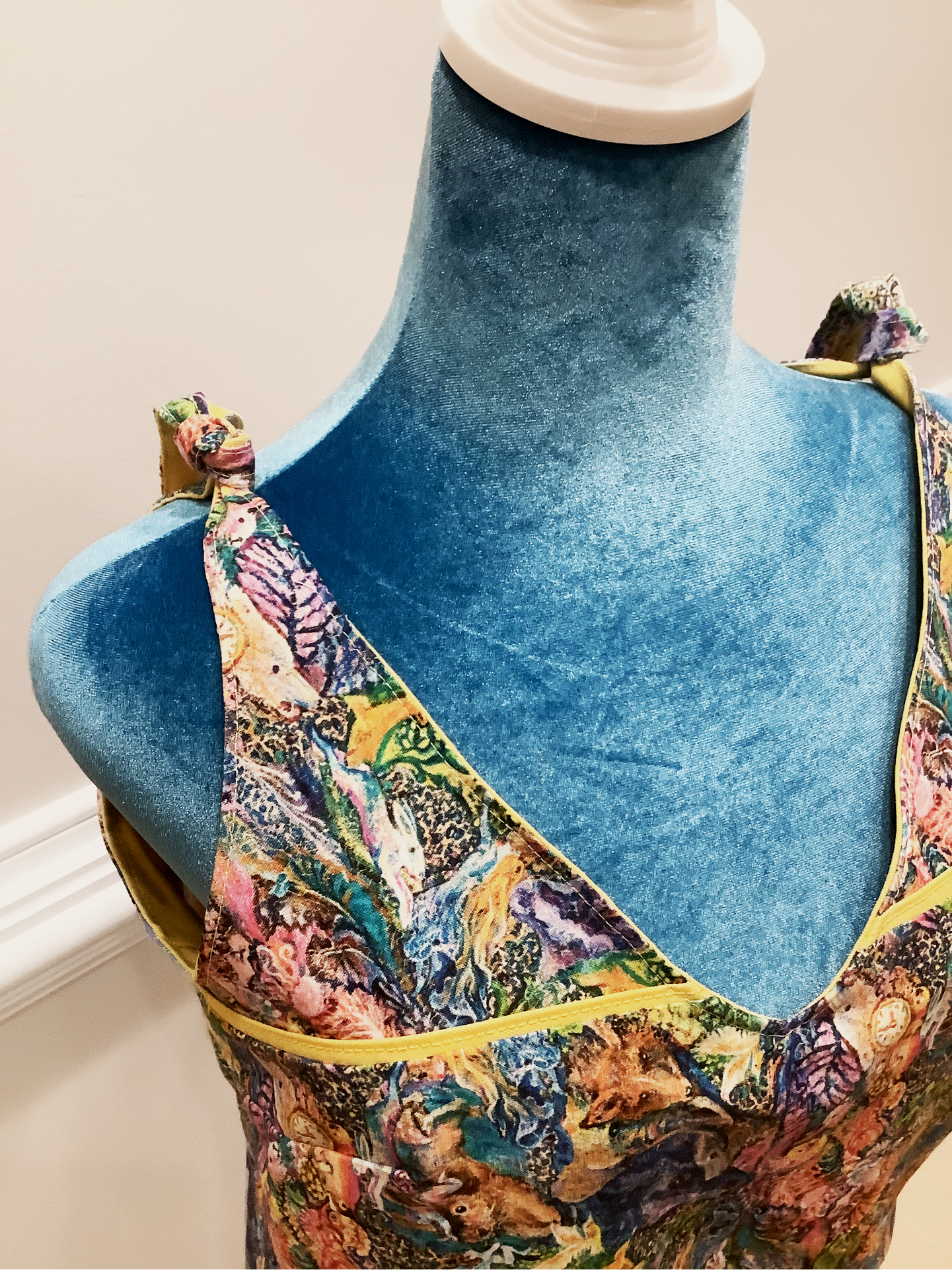Close up on the tied shoulder knots of a colorful tank top. Tank top is on a blue manniquin with a beige background.