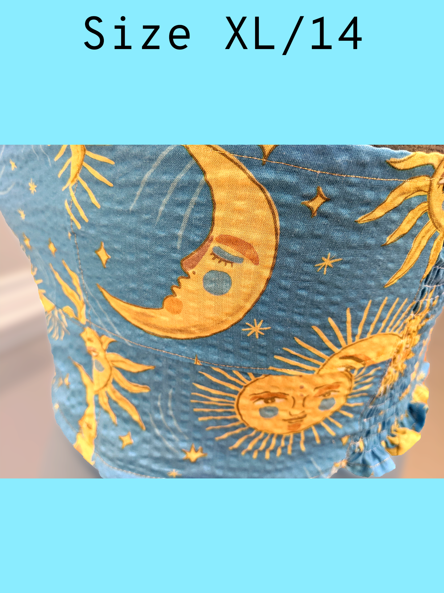 Close up side view of a light blue cropped tank top with a yellow sun and moon print and gold topstitching, displayed on a mannequin. With a text overlay that reads, "Size XL/14".